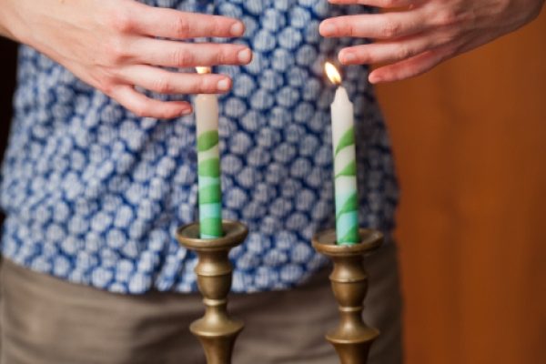 two shabbat candles are lit as someone's hands wave in the light of Shabbat