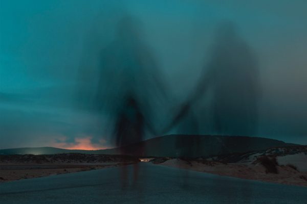 shadows-holding-hands-walking-on-dark-desert-road-toward-mountains
