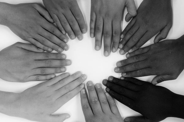 black and white photo of hands of different skin tones lying flat on a surface and arranged in a circle with fingers pointing toward the middle