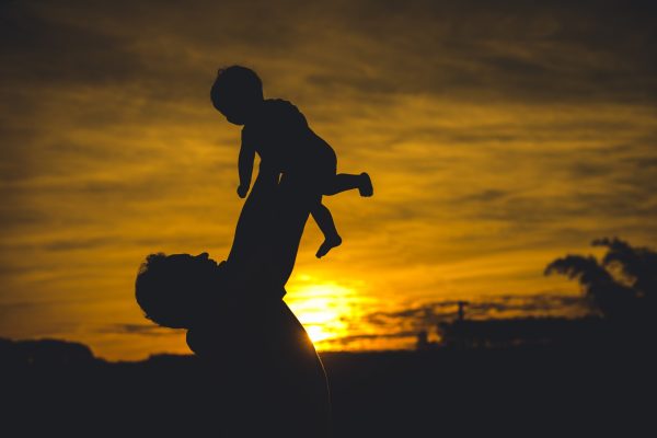 Silhouette of an adult lifting a child against a golden sunset sky.