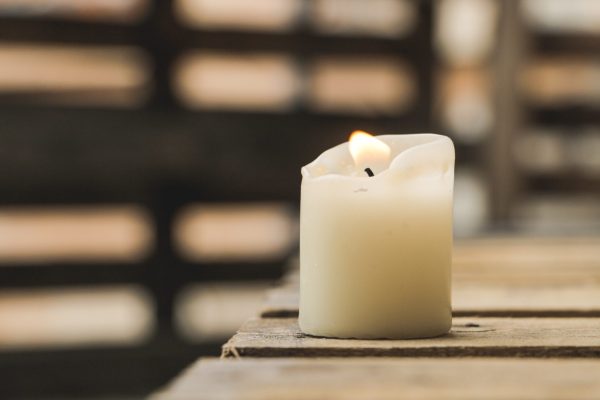 A lit white candle on a wooden table, with a blurred background.