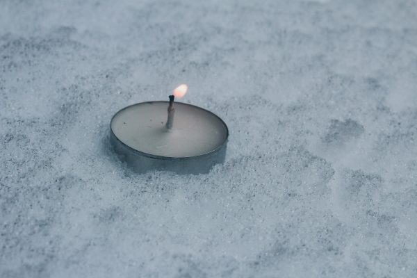 A tealight candle burning on a snowy surface.