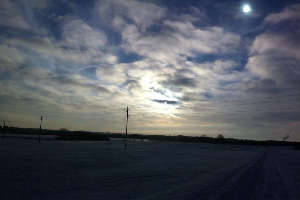 Snowy field under a cloudy sky with the sun and power lines visible in the background.