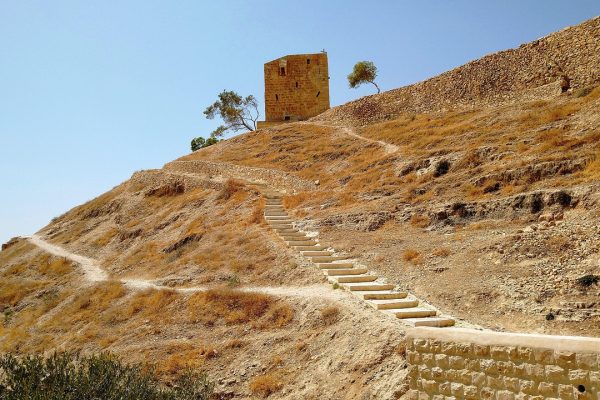 Stone stairway leading up a dry, rocky hill to a small building under a clear blue sky.