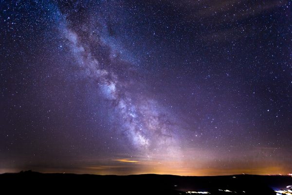 a horizon with the slight orange glow of a sun setting underneath a dark purple night sky dotted with stars and a cloud formation