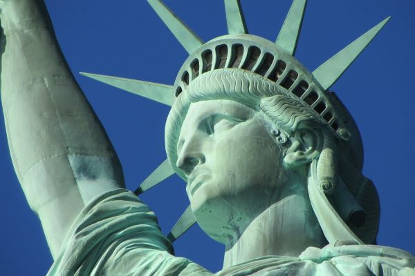 Close-up of the Statue of Liberty’s face and torch arm against a clear blue sky.