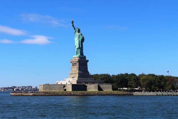 Statue of Liberty on Liberty Island, surrounded by water, with a clear blue sky in the background.