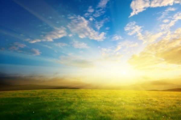 Sunrise over a green field with a blue sky and scattered clouds.