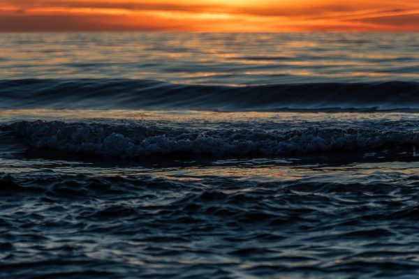 Gentle ocean waves at sunset with orange and blue reflections on the water.