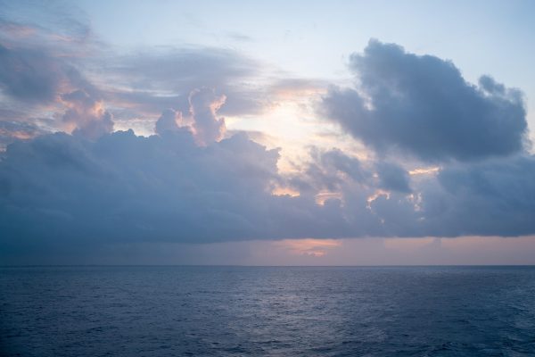Calm ocean under a cloudy sky at sunset, with soft light illuminating the clouds and horizon.
