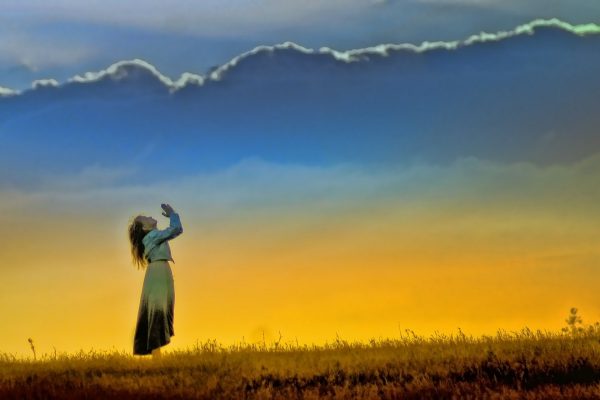 A person stands in a field, looking up at a vibrant sunset sky with dramatic clouds.