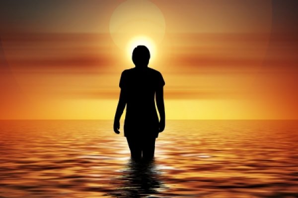 Silhouette of a person standing in water at sunset with the sun setting behind them.