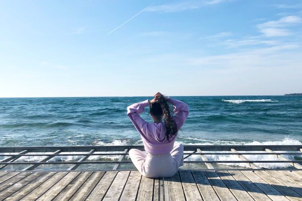 teenaged girl in sweats sitting on a pier staring at the ocean