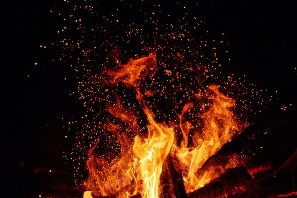 close up of bonfire flames with orange sparks flying in the air against black background