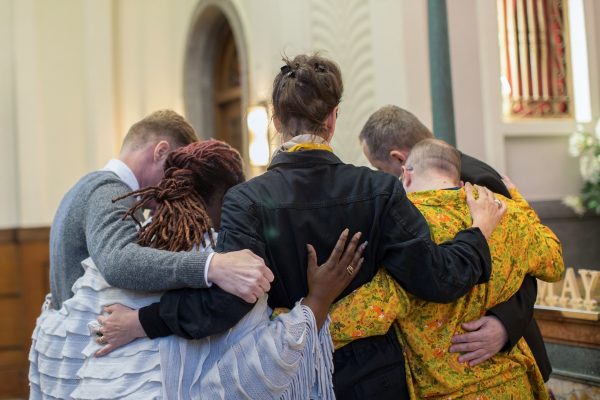 A group of people standing in a close circle, embracing each other in a church setting.