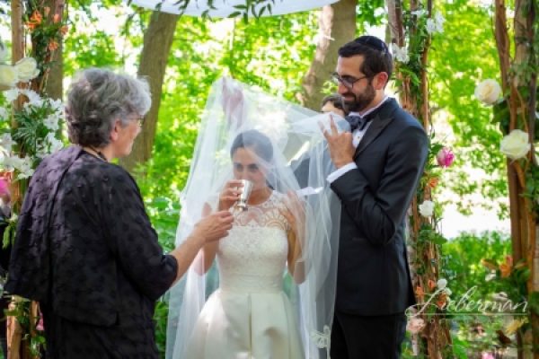 Bride and groom at an outdoor wedding ceremony, surrounded by greenery and flowers.