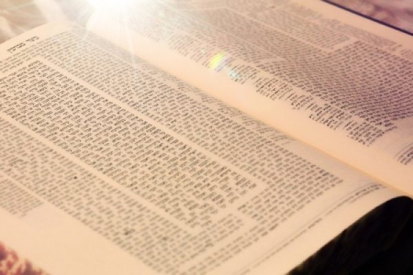 An open book with dense Hebrew text illuminated by sunlight.