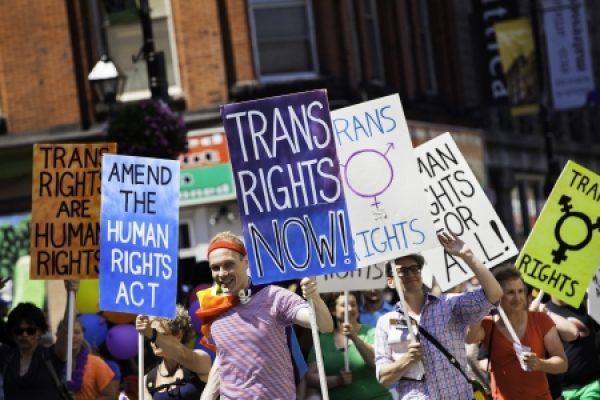 People at a pride march holding signs advocating for trans rights and equality.