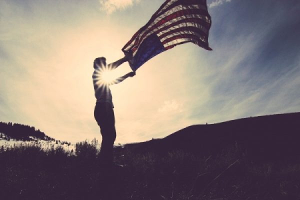 a person's silhouette waving a large American flag under a bright sky