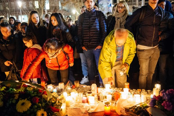 group of people outside at candlelit vigil - two people shown leaning down lighting candles