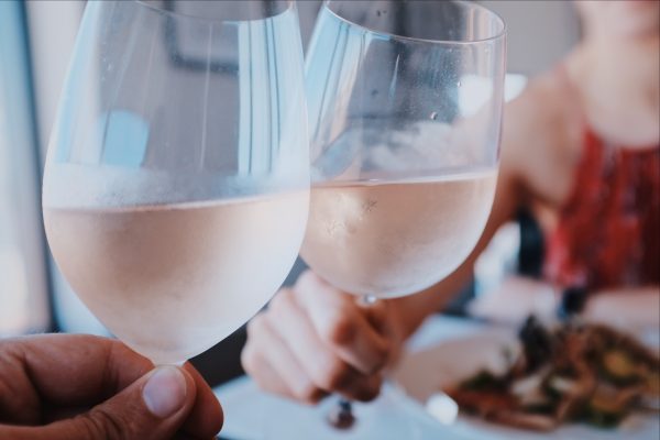 Two people clinking glasses of chilled white wine over a meal, with a blurred background.