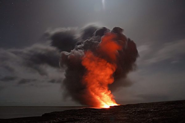 Volcanic eruption at night with bright lava and dark smoke billowing under a starry sky.