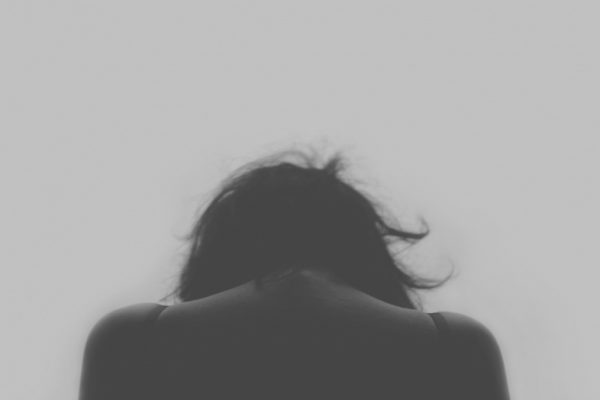 Silhouette of a person with head bowed and messy hair against a plain background.