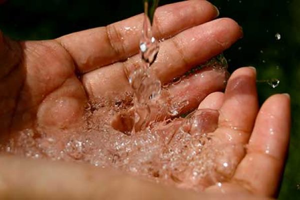 Water pouring into cupped hands, with droplets splashing and glistening in the light.