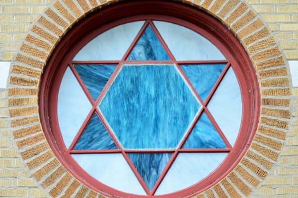 Circular stained glass window with a blue Star of David, set in a brick wall.