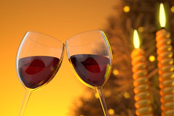 Two glasses of red wine clinking against a warm golden background with lit candles.