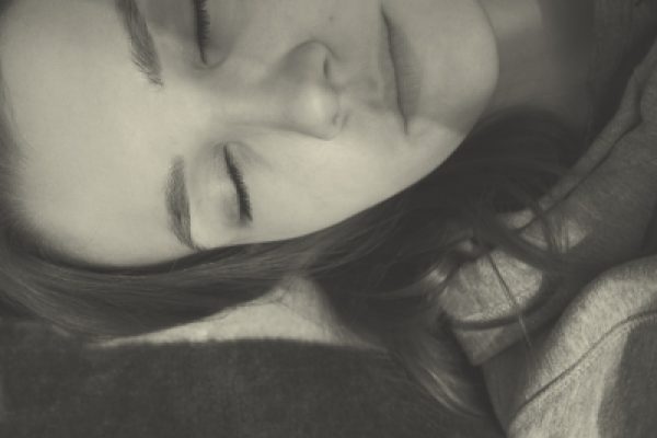 Close-up of a person with closed eyes, resting on a pillow. Black and white image with soft lighting.