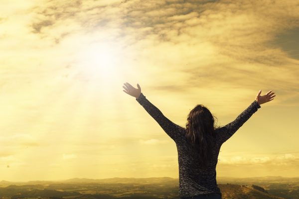 a woman opens her arms towards the sunny sky