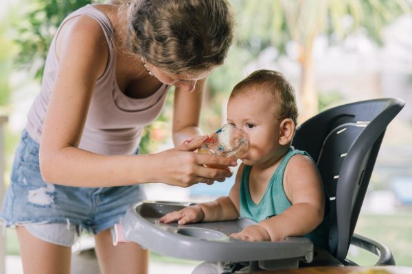 woman helping toddler drink from cup