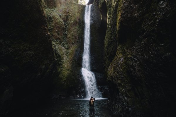 woman standing in a canyon stream facing a waterfall