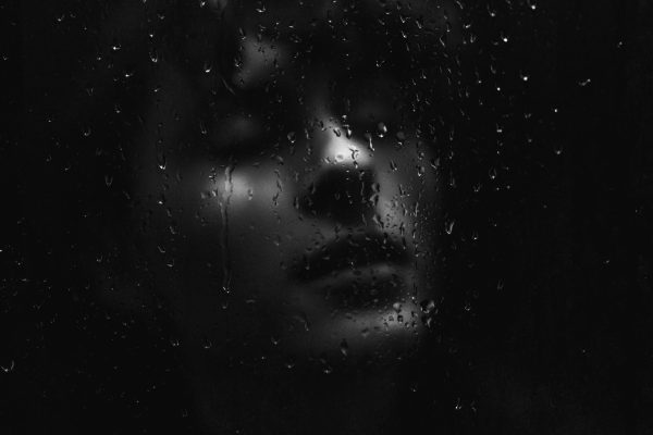 woman in dark behind window with raindrops