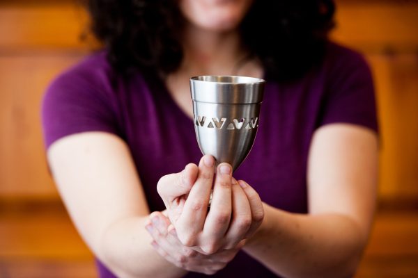 Person in a purple shirt holding a stainless steel cup with heart cutouts.