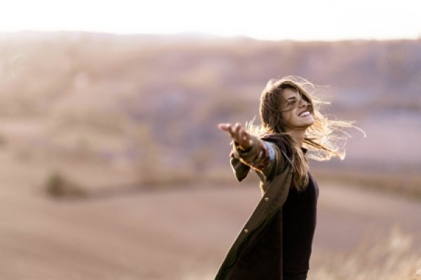 Woman joyfully extending arms in a sunlit open field, with long hair blowing in the breeze.