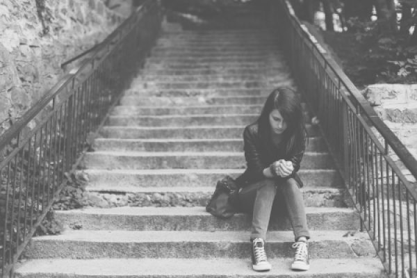 A person sitting on outdoor steps, looking down, in a black and white photo.