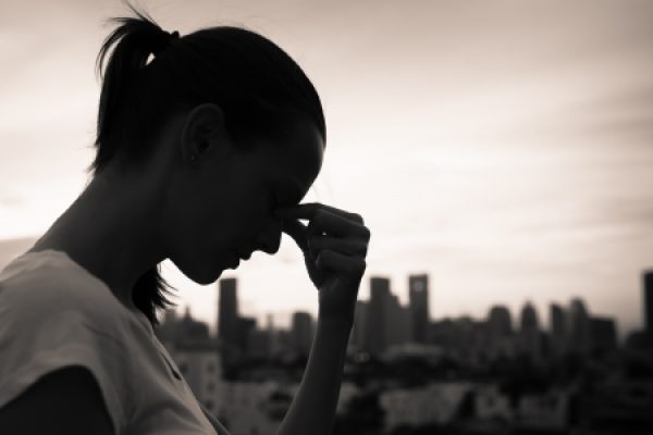 Silhouette of a person with a headache, holding their forehead, set against a cityscape at sunset.