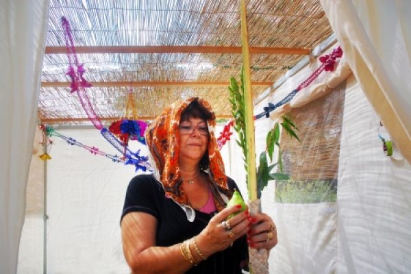 Person holding a lulav and etrog in a decorated sukkah.
