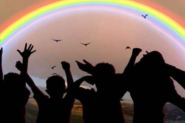 a group of children holding hands below a rainbow