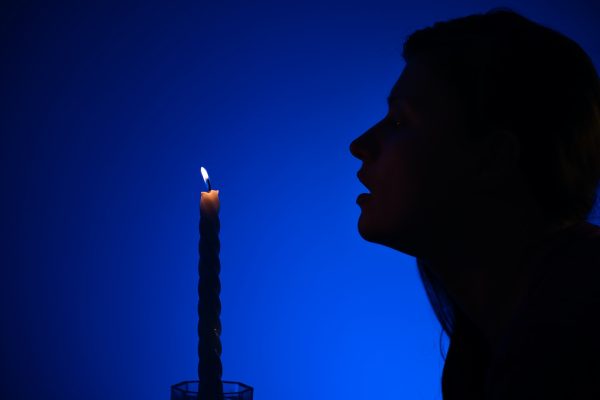 Silhouette of a person blowing out a candle against a vivid blue background.