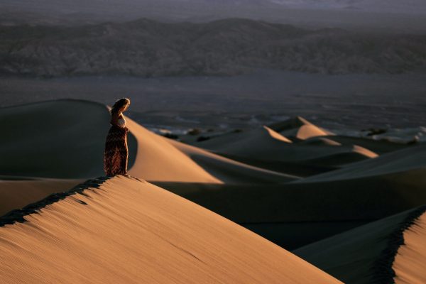woman in a desert with mounds of sand shown with shadows. she is small and far away in the scene.
