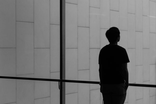 Silhouette of a person standing by a large window with a tiled wall background, looking outside.