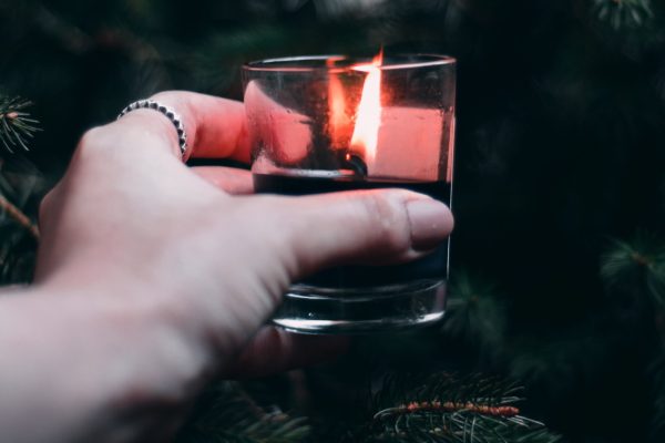 close up of white hand holding lit candle in glass holder