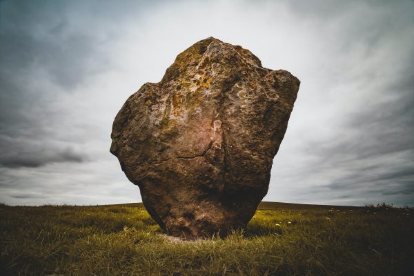 A large standing stone on grass under a cloudy sky.